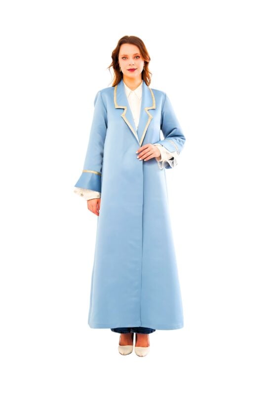 Model wearing the celeste opulence overcoat: a tailored sky-blue wool-satin blend coat with metallic gold piping along the lapels and cuffs, featuring a tone-on-tone art deco jacquard back panel and removable self-fabric belt.