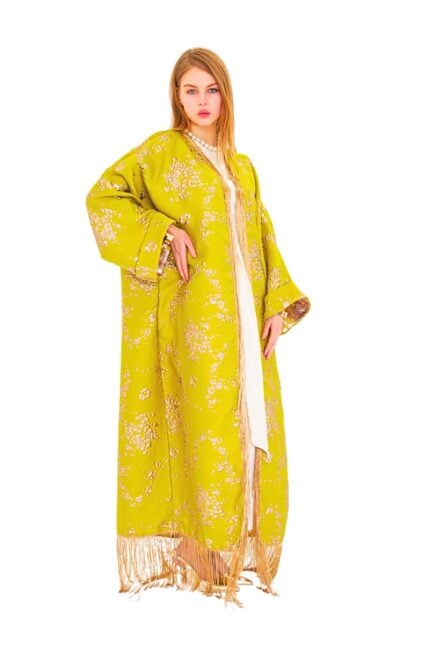 Model wearing the Lime Bloom Fringed Kaftan: a flowing lime-green silk-blend jacquard kaftan with tonal floral motif, wide kimono sleeves, gold-beige fringe along hem and cuffs, and a removable self-fabric sash.