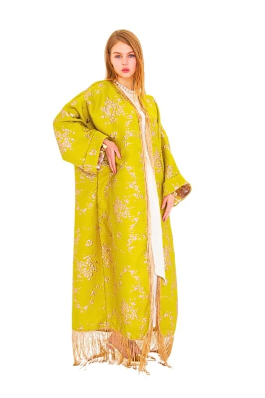 Model wearing the lime bloom fringed kaftan: a flowing lime-green silk-blend jacquard kaftan with tonal floral motif, wide kimono sleeves, gold-beige fringe along hem and cuffs, and a removable self-fabric sash.