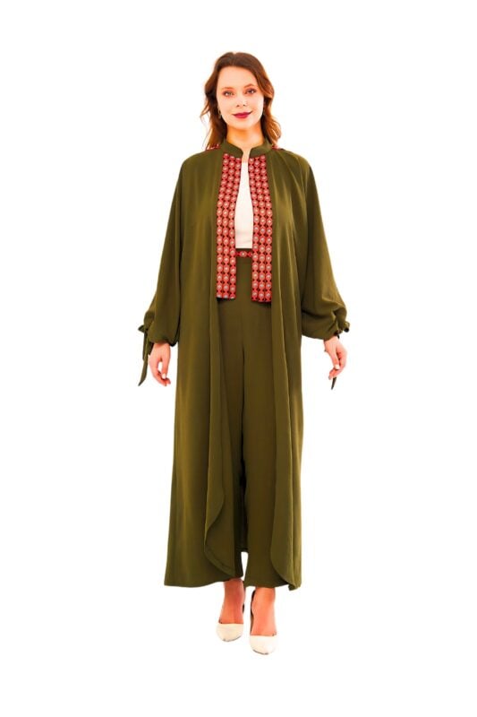Model wearing the nomadic charm two-piece set: an olive-green flowing duster coat with tie-cuff sleeves layered over matching high-waist wide-leg trousers, featuring a contrasting rust geometric embroidered front panel and styled with a white blouse.